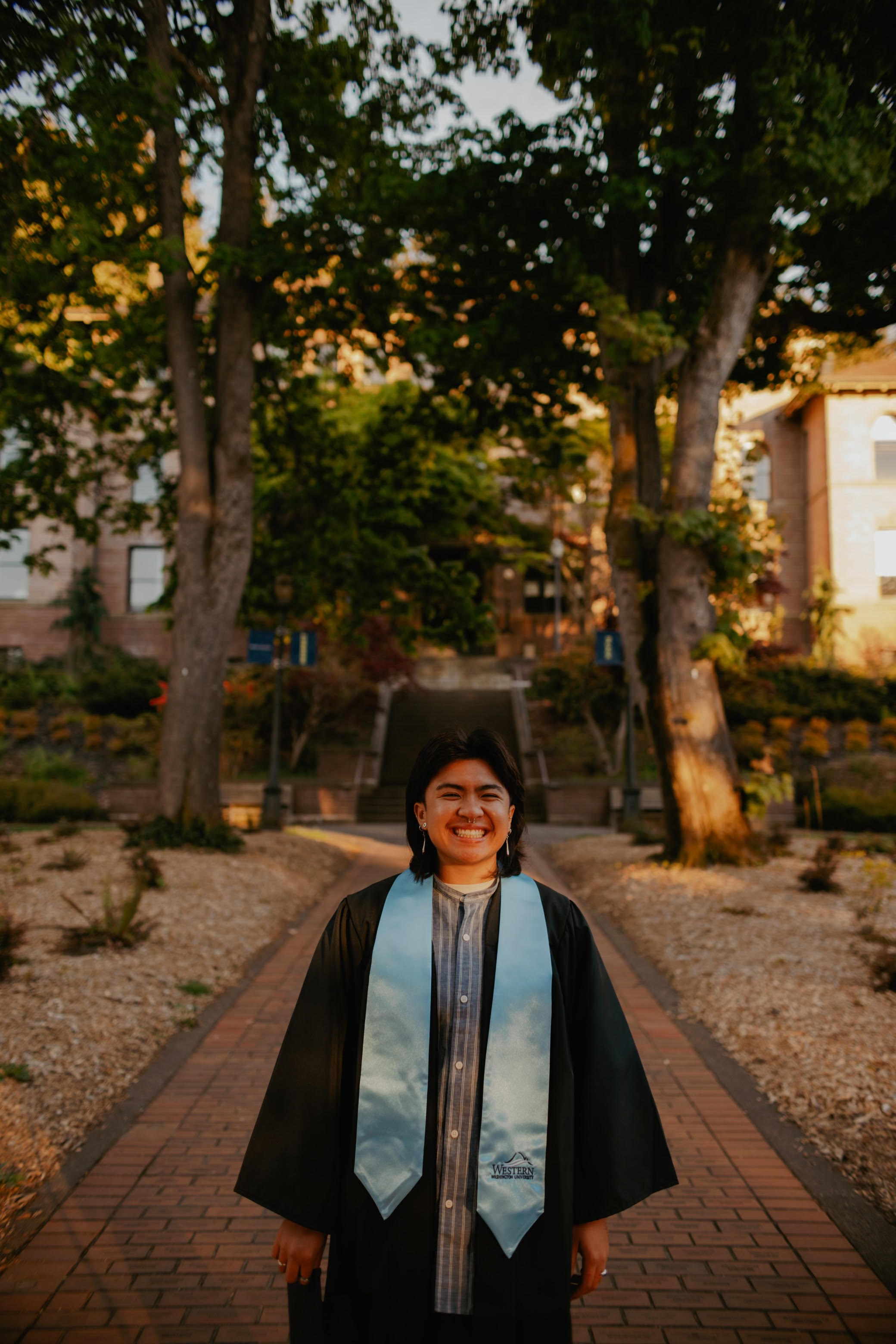 Sof standing in front of Old Main wearing their regalia, a black gown with blue stole
